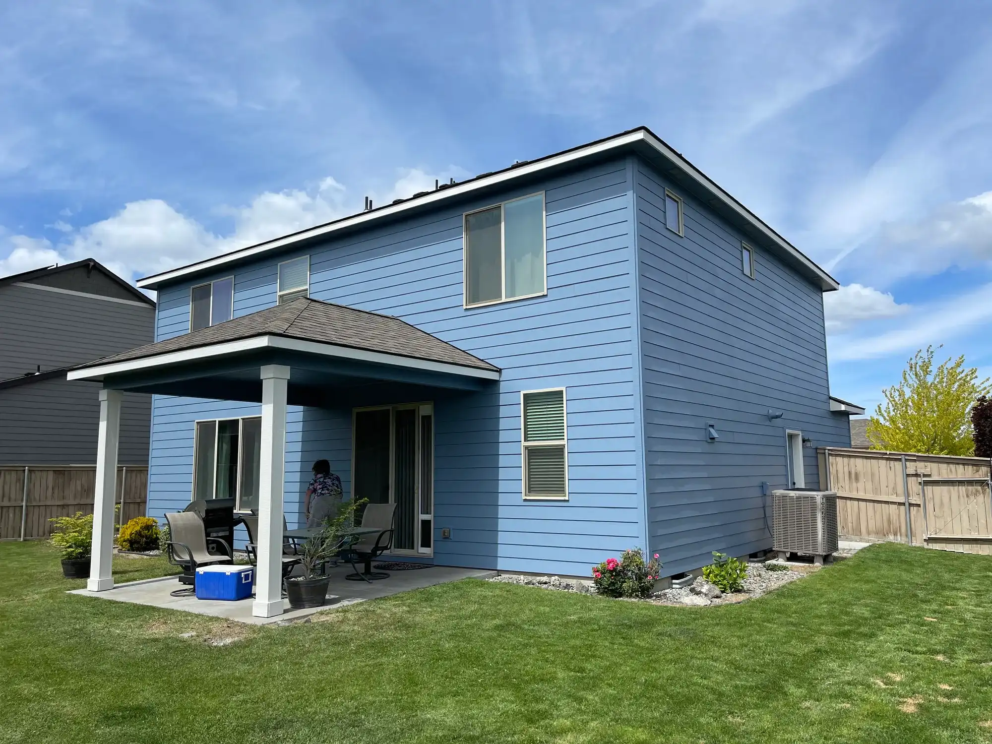 Two-story home freshly painted blue with white trim, seen from the backyard with its covered patio