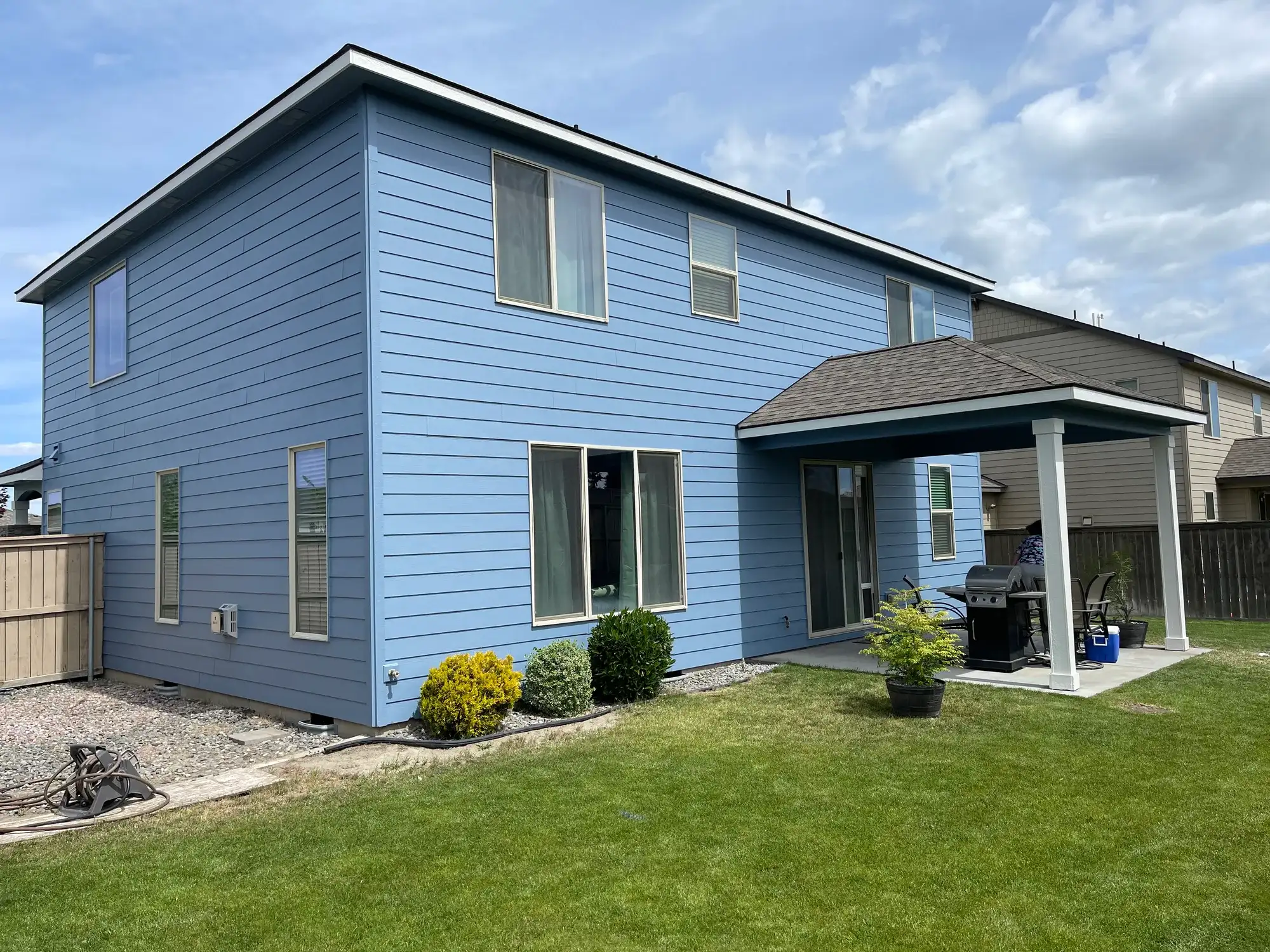 Side of a home painted blue with white trim and a covered back patio