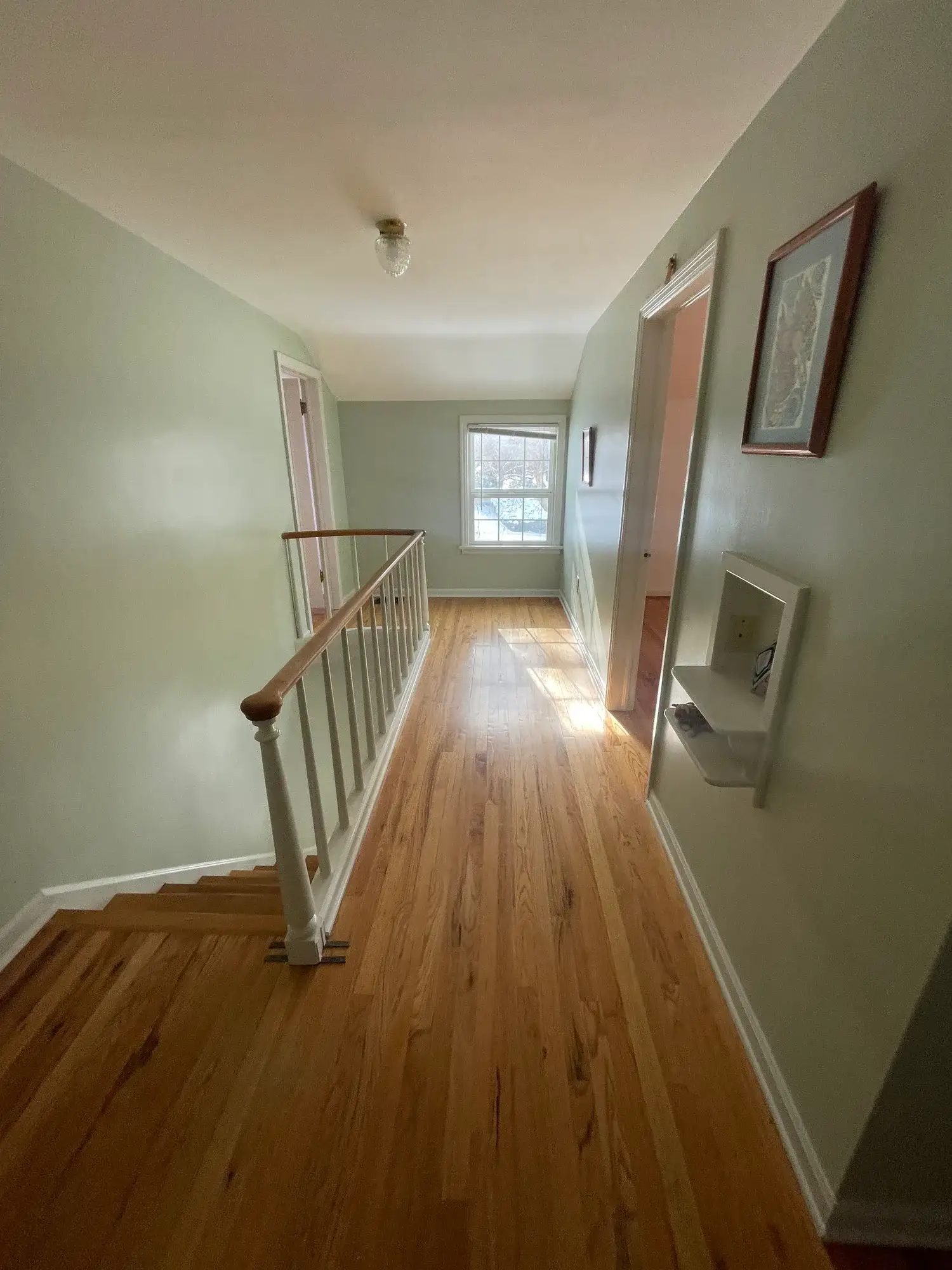 Upstairs hallway with freshly painted light green walls, white trim and wood floors