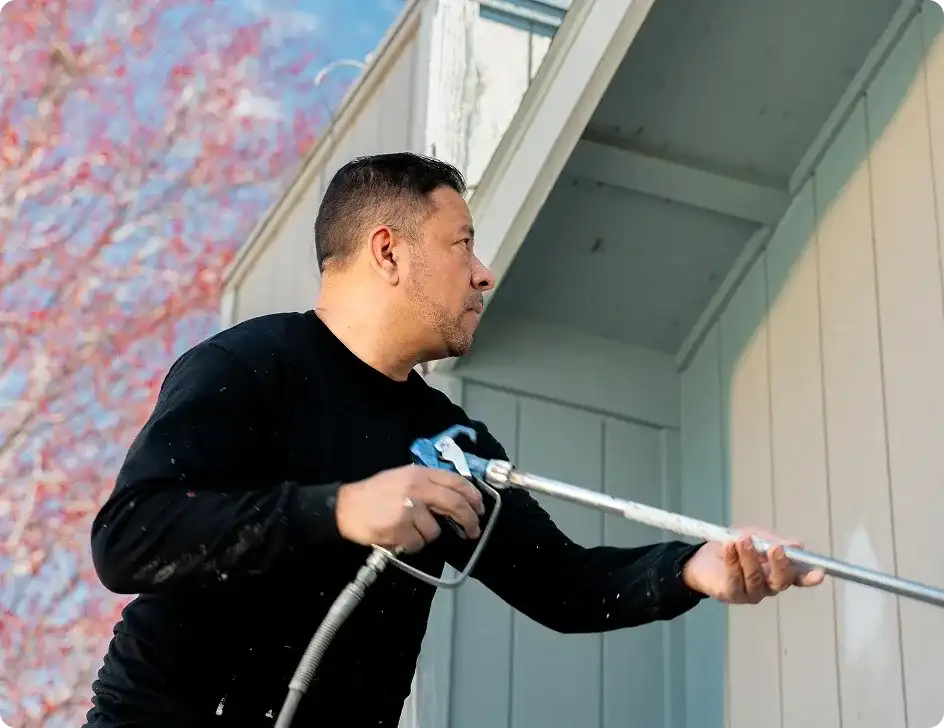 Casa Vida painter spraying light siding under the eaves