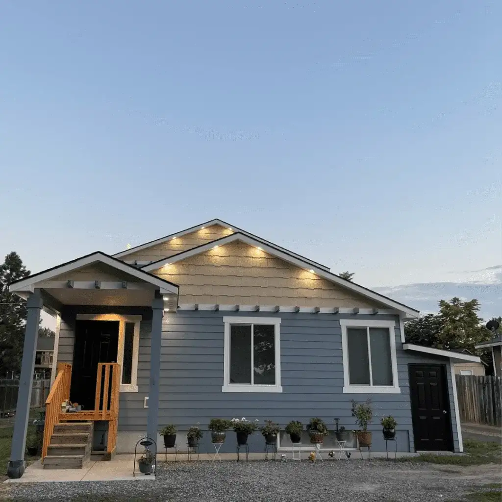Front of a slate-blue home with white trim, lights under the eaves and new wood entry steps