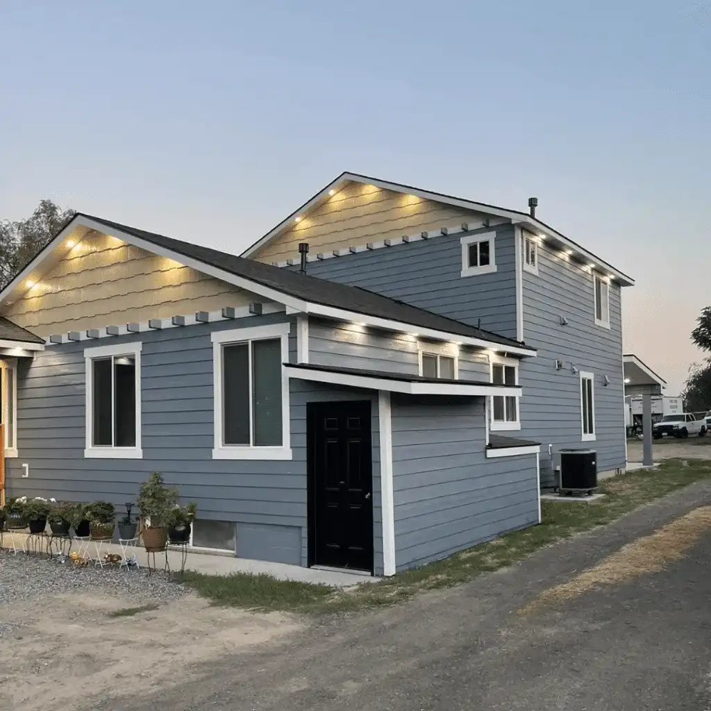 Slate-blue home at dusk with white trim and lights glowing under the eaves