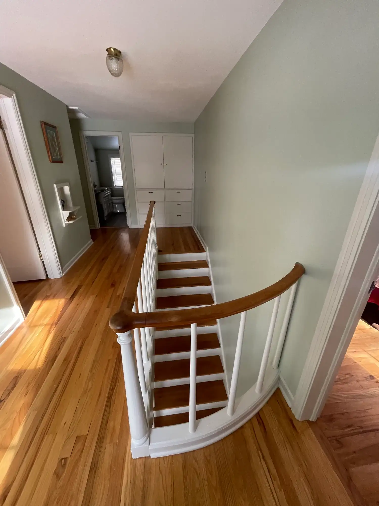 Refinished wood stairs with white risers and a curved wood handrail, seen from the top